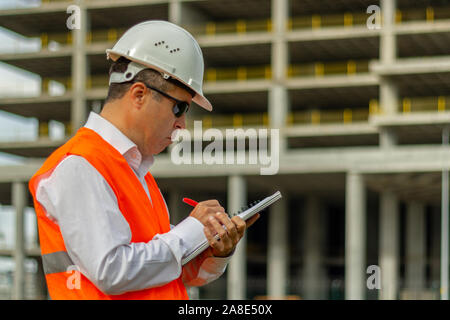 Construction engineer man in shirt and tie with safety helmet and vest works at construction site. Concept of people working in industrial field Stock Photo