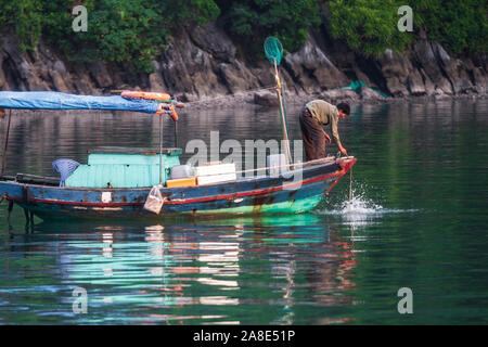 Ha Long Bay, Vietnam - 17th October 2019: A fisherman fishes from the side of his wooden boat near Cat Ba Village in Ha Long Bay, Vietnam Stock Photo