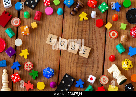 'Lose' spelled out in wooden letter tiles. Surrounded by dice, cards, and other game pieces on a wooden background Stock Photo