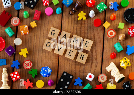 "Game Over" spelled out in wooden letter tiles. Surrounded by dice, cards, and other game pieces on a wooden background Stock Photo
