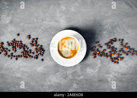 Gray concrete background with white cup of tasty coffee surrounded by coffee beans. Flat lay, top view, copy space. Stock Photo