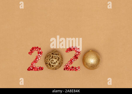 2020 made of red sparkles and decorative golden christmas ballls on craft sheet of paper. Happy new year 2020 concept. Stock Photo