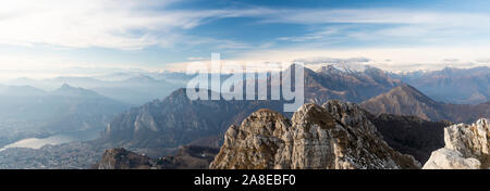 Panoramic view of the city of Lecco (Lombardy, Italy) and of the nearby mountains from the summit of Mount Resegone on a winter day with mist. Stock Photo