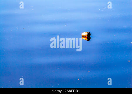 A coffee cup with a plastic lid lies on its side, floating in the water of a river. The water reflects the image of the red cup and its single-use lid Stock Photo