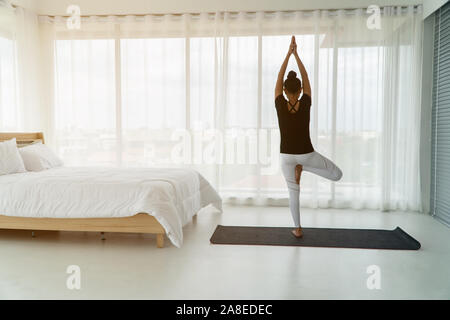 Middle aged women doing yoga in bedroom at the morning, adho mukha svanasana pose. Concept of exercise and relaxation in the morning.