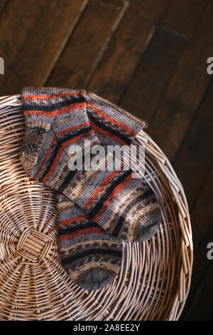 A pair of hand knitted multi-colored socks on a pad. Dark rustic wooden background. Plase for text. Stock Photo