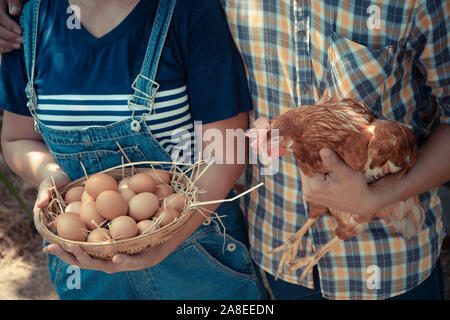 Couple farmer holding fresh chicken eggs into basket and holding  hen beside chicken farm. Concept of Non-toxic food Stock Photo
