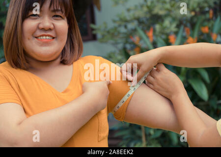 Overweight woman in the park and measuring the proportion to the upper arm she smalling because she lost weight And can be proportional down. Concept Stock Photo