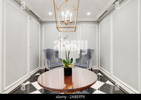 Close up of a gray waiting room area with two chairs, an orchid sitting on the table and a gold light hanging from the ceiling. Stock Photo
