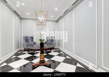 Close up of a gray waiting room area with two chairs, an orchid sitting on the table and a gold light hanging from the ceiling. Stock Photo