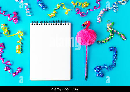 Goals list for New Year. Christmas party set with with wish list notebook, pen in form of flamingo and multi colored confetti on blue green color background. Flat lay top view. Planning concept. Stock Photo