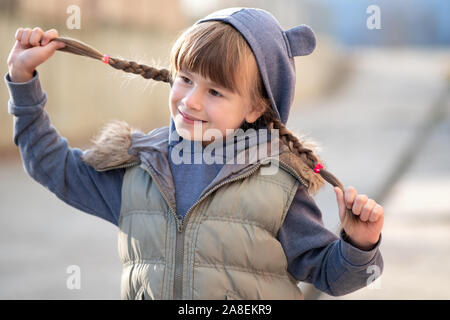 Portrait of happy child girl with hair braids in warm clothes in autumn outdoors. Stock Photo