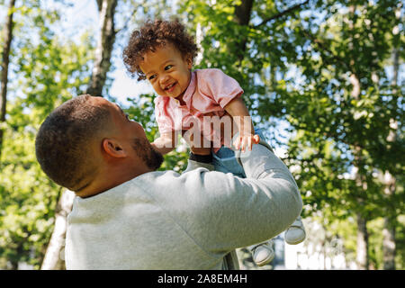 Young dad having fun with toddler son lifting up high outdoors Stock Photo