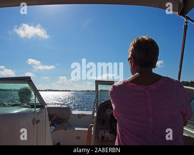 Woman at the helm of pleasure boat on Southwest Florida's Intracoastal Waterway, Florida, USA, October 30, 2019, © Katharine Andriotis Stock Photo