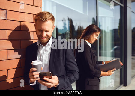 A bearded businessman is drinking coffee while sitting on a city street Stock Photo