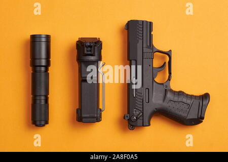 self defense gear - pistol, pepper spray and tactical flashlight on orange background Stock Photo