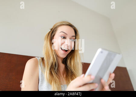 Jocund girl using tablet and sitting in bed. Stock Photo