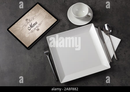 Tablet with stylish restaurant logo and laid table Stock Photo