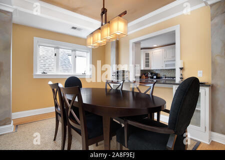 A small dining room in a condo that is overlooked by a window from the kitchen. A dark table and chairs is centered under a modern light fixture. Stock Photo