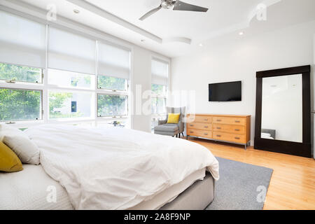 Master bedroom in a modern home with yellow accents to make the neutral colors pop within the large room. Stock Photo