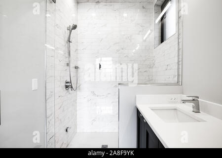 A luxurious bathroom with white granite over a dark vanity and a white marble tiled shower with glass walls and door. Stock Photo