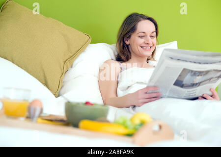25 -30 jährige Frau schläft im Bett und liest die Zeitung,  MR:Yes