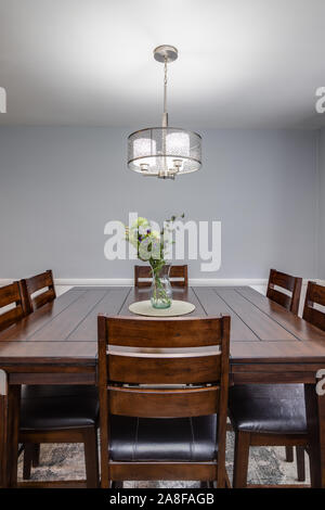Detail shot of a small dining room with a cherry wood table, flowers as a centerpiece and a light hanging from the ceiling. Stock Photo