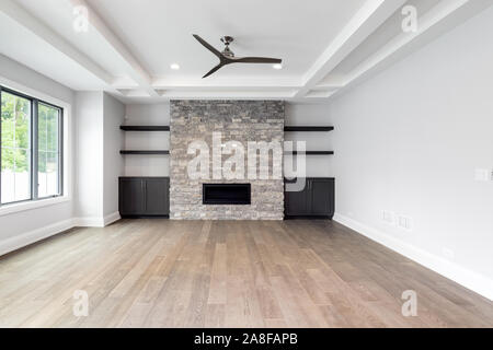 A modern, updated empty living room area with hardwood floors, a brick fireplace surrounded by shelves and cabinets, and a backyard view. Stock Photo