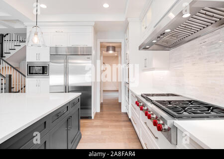 A luxurious modern kitchen with stainless steel Wolf appliances surrounded by white cabinets, beautiful granite, and hardwood floors. Stock Photo