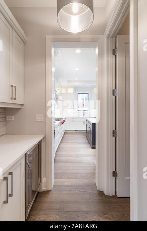 Looking through a hallway with a pantry, a wine fridge under the cabinets, and towards the luxurious white kitchen. Stock Photo