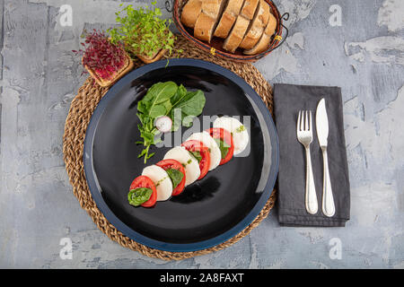 Cheese plate with mozzarella; Plate of healthy classic delicious caprese salad with ripe tomatoes and mozzarella cheese with fresh arugula leaves on b Stock Photo