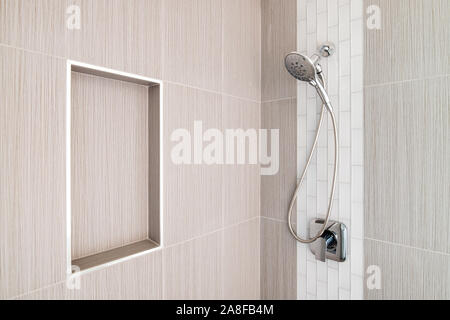A detail shot of a beautifully tiled shower with brown large tiles,white subway tiles, and a shelf cut out for amenities. Stock Photo