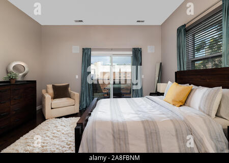 A cozy master bedroom in a downtown Chicago condo with a sliding door leading to a balcony. Stock Photo