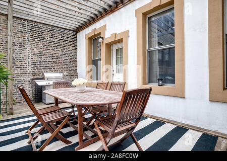 A patio in a downtown condo with a large wooden table, chairs and a stainless steel grill. Stock Photo