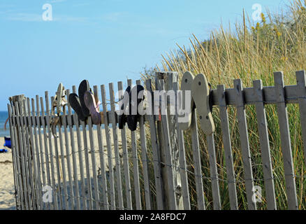 Flip-flops adorning a rickety wooden fence protecting dunes along the sandy path entrance to Nauset Light Beach on Cape Cod in Eastham, Massachusetts Stock Photo
