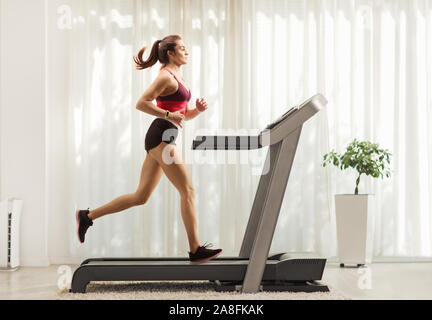 Full length profile shot of a young woman running on a treadmill at home Stock Photo
