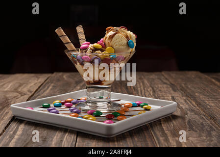 Vanilla ice cream in a sundae glass bowl with rolled wafer sticks and chocolate sauce on wooden background Stock Photo