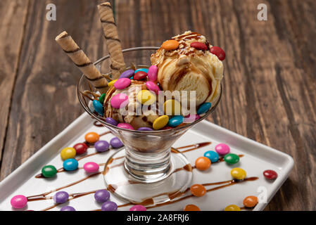 Vanilla ice cream in a sundae glass bowl with rolled wafer sticks and chocolate sauce on wooden background Stock Photo