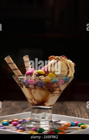 Vanilla ice cream in a sundae glass bowl with rolled wafer sticks and chocolate sauce on wooden background Stock Photo