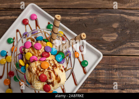 Vanilla ice cream in a sundae glass bowl with rolled wafer sticks and chocolate sauce on wooden background Stock Photo