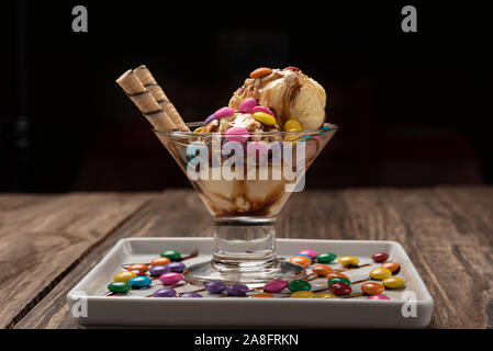 Vanilla ice cream in a sundae glass bowl with rolled wafer sticks and chocolate sauce on wooden background Stock Photo