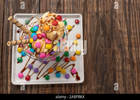 Vanilla ice cream in a sundae glass bowl with rolled wafer sticks and chocolate sauce on wooden background Stock Photo