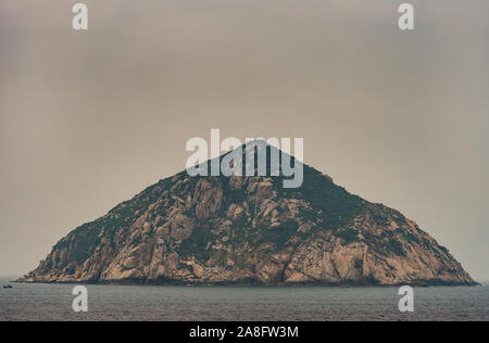 Nha Trang, Vietnam - March 11, 2019: Closeup of Rock island in South China Sea at entrance to harbor of the town. Foggy morning sky and gray blue sea Stock Photo