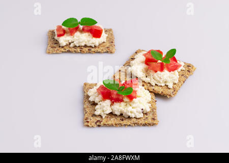 Diet flax seed whole grain crackers with ricotta cheese, tomato and herbs isolated on white background, soft light Stock Photo