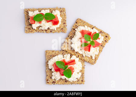 Diet flax seed whole grain crackers with ricotta cheese, tomato and herbs isolated on white background, soft light Stock Photo