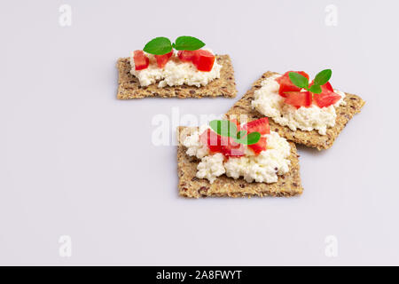 Diet flax seed whole grain crackers with ricotta cheese, tomato and herbs isolated on white background, soft light Stock Photo