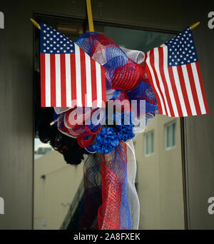 Two small American flags incorporated into a red, white and blue ribboned wreath on glass door, in the USA Stock Photo