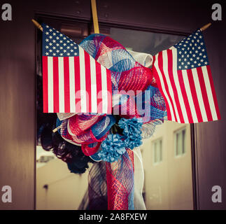 Two small American flags incorporated into a red, white and blue ribboned wreath on glass door, in the USA Stock Photo