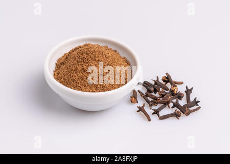 Ground cloves in white ceramic bowl isolated on white background, soft light, studio shot, copy space. Whole cloves. Stock Photo