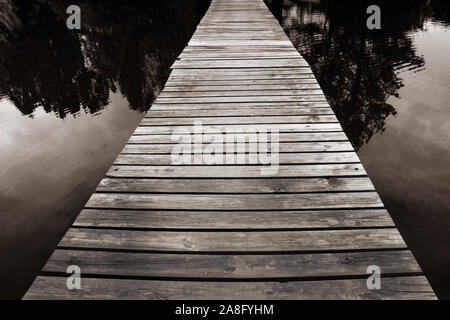 A mystical seeming wooden footbridge crosses the water at twilight with trees reflecting in water for a zen experience Stock Photo